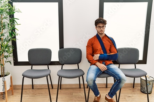 Young hispanic man injuried sitting on chair at clinic waiting room