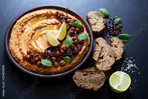 Hummus with sun-dried tomatoes on a brown plate. Healthy and delicious food