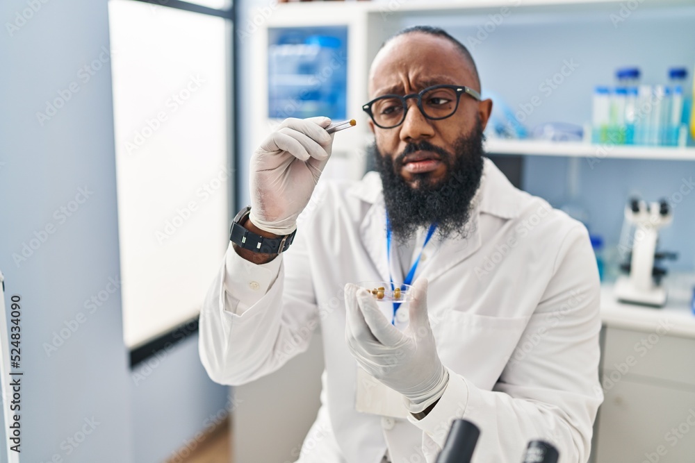 Fototapeta premium Young african american man wearing scientist uniform using tweezer at laboratory