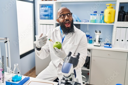 African american man working at scientist laboratory with apple angry and mad screaming frustrated and furious  shouting with anger looking up.
