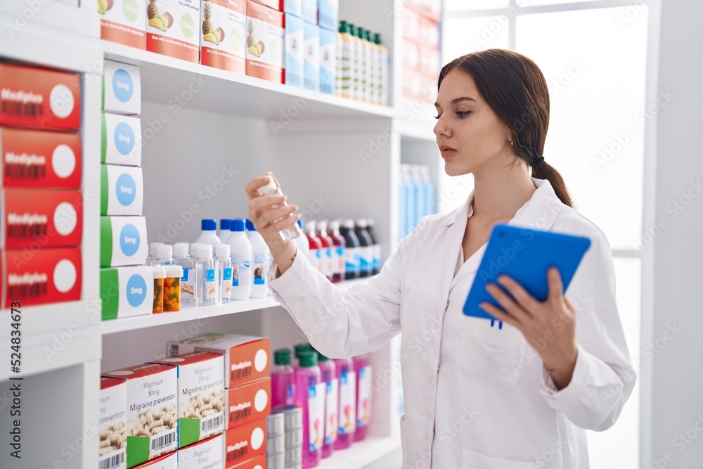 Young woman pharmacist using touchpad holding bottle at pharmacy