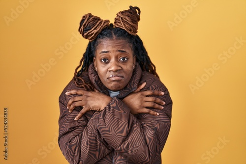 African woman with braided hair standing over yellow background shaking and freezing for winter cold with sad and shock expression on face © Krakenimages.com