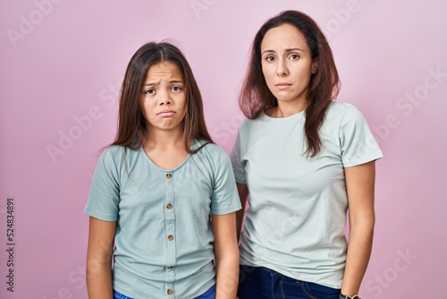 Young mother and daughter standing over pink background depressed and worry for distress, crying angry and afraid. sad expression.