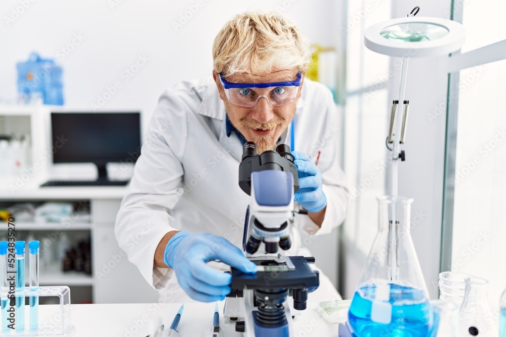 Young caucasian man wearing scientist uniform using microscope at laboratory Young caucasian man wearing scientist uniform using microscope at laboratory