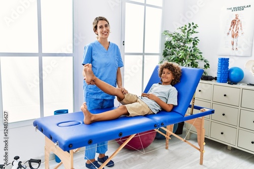 Mother and son wearing physiotherapist uniform having rehab session stretching leg at physiotherapy clinic © Krakenimages.com