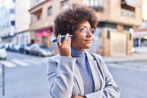 African american woman executive listening voice message by smartphone at street