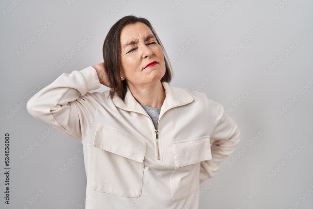 Middle age hispanic woman standing over isolated background suffering of neck ache injury, touching neck with hand, muscular pain Middle age hispanic woman standing over isolated background suffering of neck ache injury, touching neck with hand, muscular pain