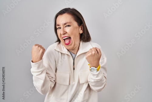 Middle age hispanic woman standing over isolated background very happy and excited doing winner gesture with arms raised, smiling and screaming for success. celebration concept.
