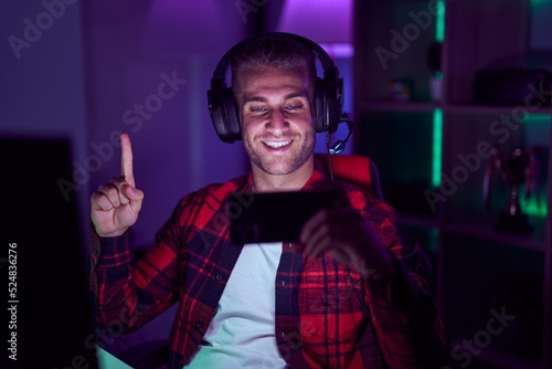 Young caucasian man playing video games with smartphone smiling with an idea or question pointing finger with happy face, number one