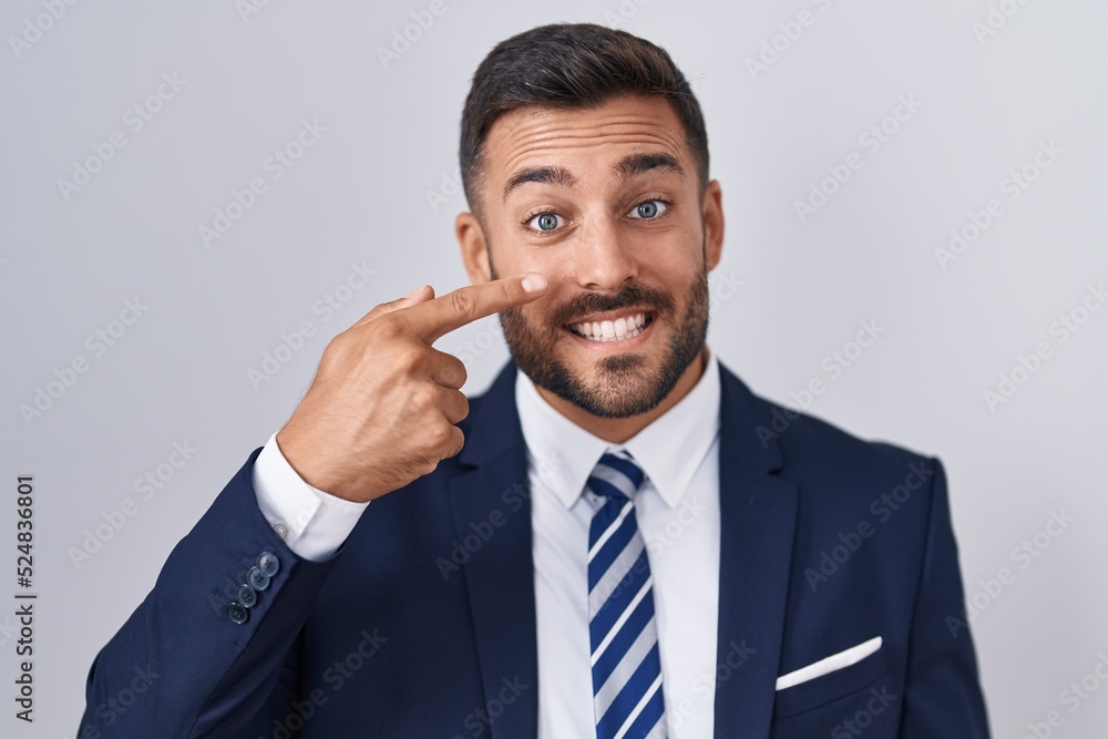 Handsome hispanic man wearing suit and tie pointing with hand finger to face and nose, smiling cheerful. beauty concept Handsome hispanic man wearing suit and tie pointing with hand finger to face and nose, smiling cheerful. beauty concept