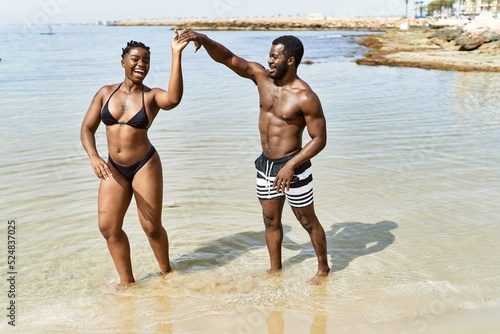 Young african american tourist couple wearing swimwear dancing at the beach.