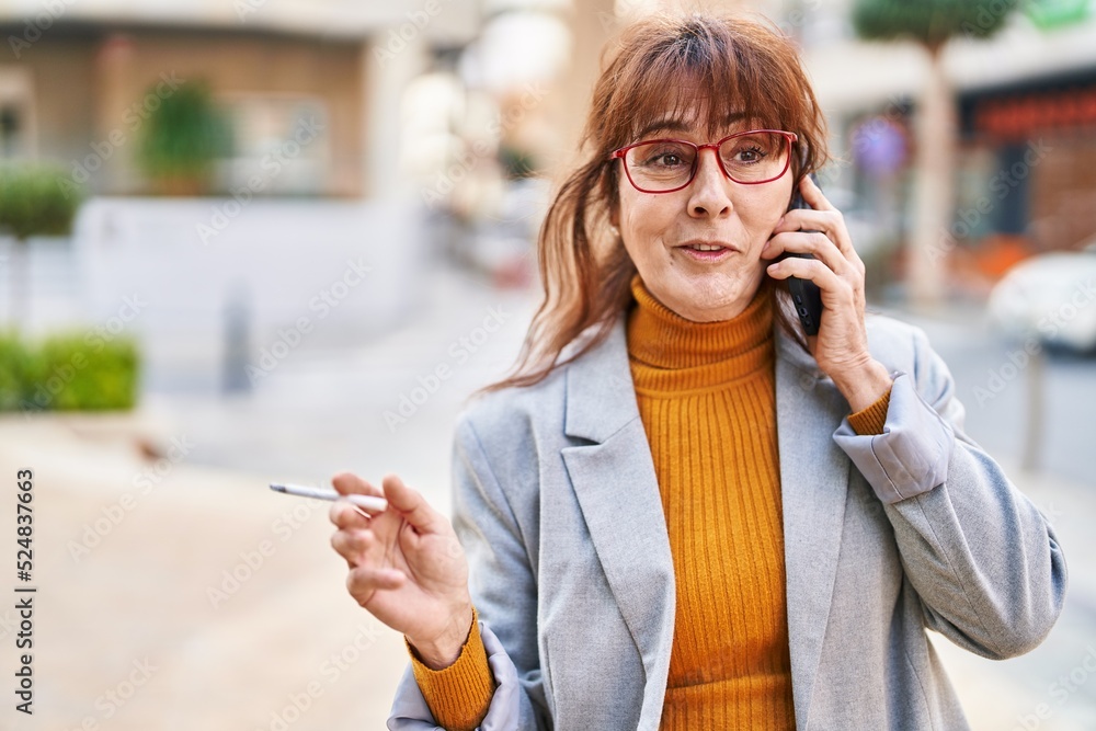 Middle age woman business executive talking on the smartphone smoking cigarette at street Middle age woman business executive talking on the smartphone smoking cigarette at street