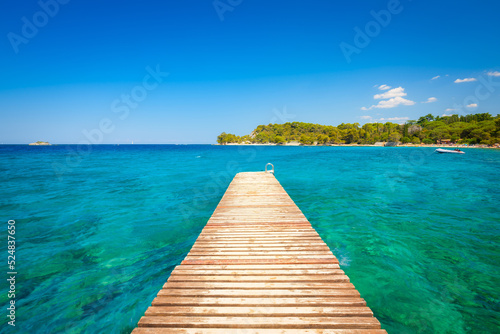 Pier at sea in the summertime. Azure sea and shore with rocks. Clear sea water and clear sky. Adriatic Sea, Croatia.