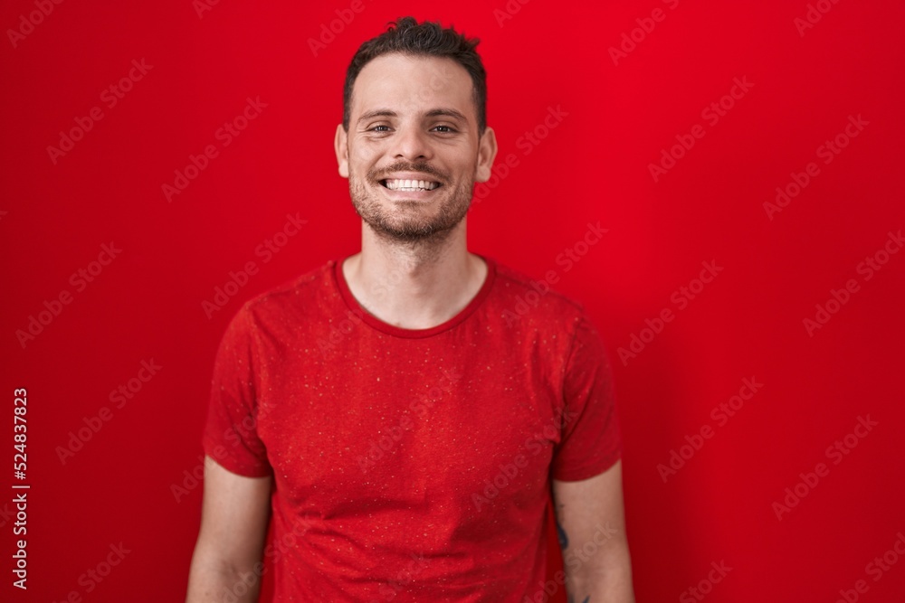 Young hispanic man standing over red background with a happy and cool smile on face. lucky person. Young hispanic man standing over red background with a happy and cool smile on face. lucky person.
