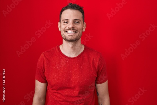 Young hispanic man standing over red background with a happy and cool smile on face. lucky person.