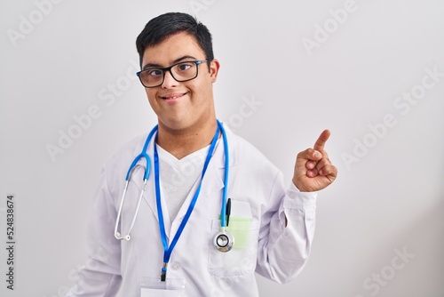 Young hispanic man with down syndrome wearing doctor uniform and stethoscope pointing finger up with successful idea. exited and happy. number one.