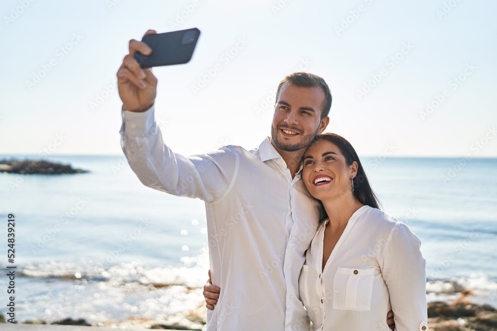 Man and woman couple hugging each other make selfie by the smartphone standing at seaside