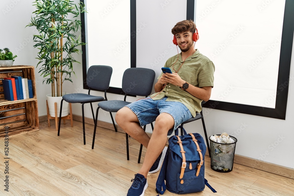 Young arab man listening to music sitting on the chair at waiting room
