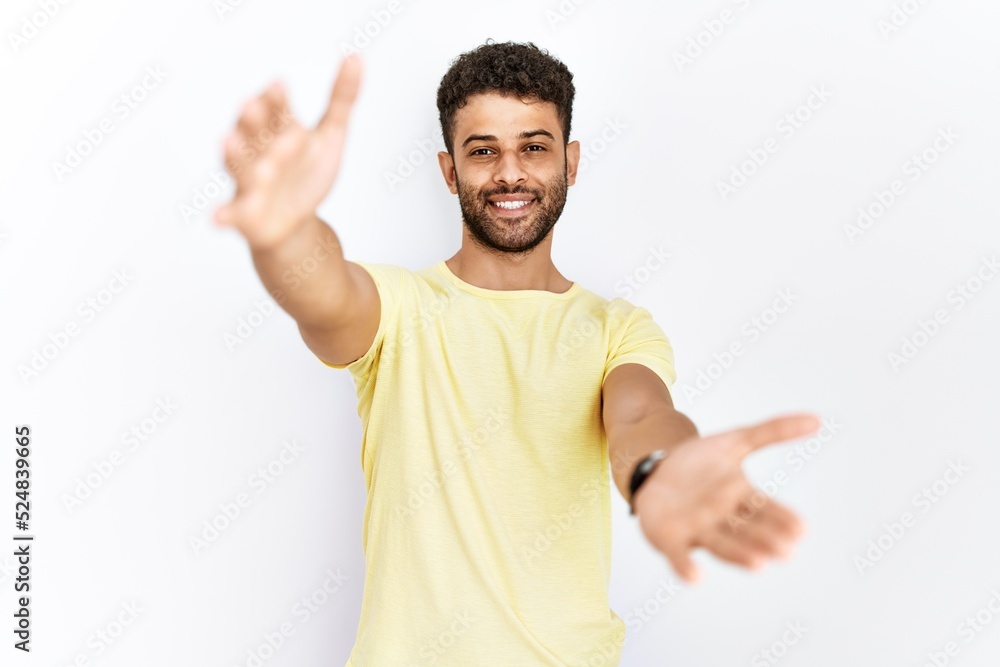 Arab young man standing over isolated background looking at the camera smiling with open arms for hug. cheerful expression embracing happiness. Arab young man standing over isolated background looking at the camera smiling with open arms for hug. cheerful expression embracing happiness.