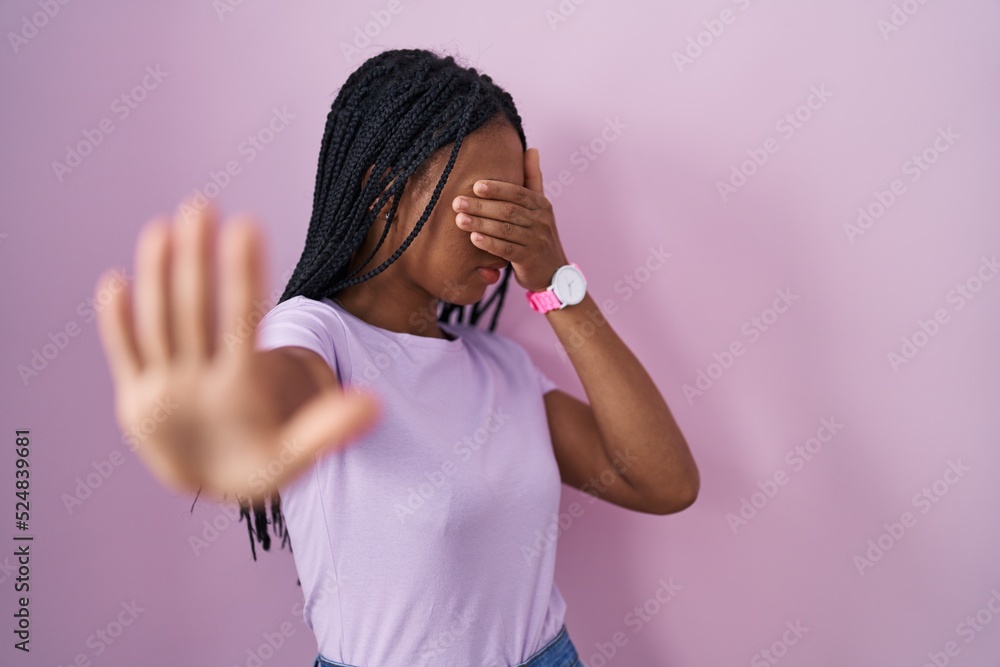 African american woman with braids standing over pink background covering eyes with hands and doing stop gesture with sad and fear expression. embarrassed and negative concept. African american woman with braids standing over pink background covering eyes with hands and doing stop gesture with sad and fear expression. embarrassed and negative concept.