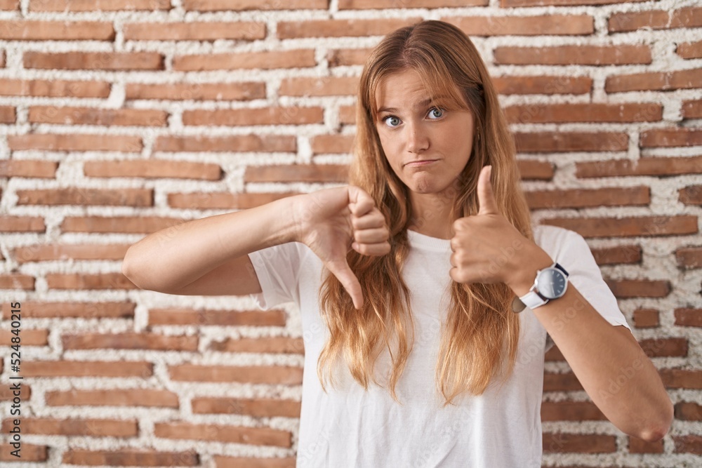 Young caucasian woman standing over bricks wall doing thumbs up and down, disagreement and agreement expression. crazy conflict Young caucasian woman standing over bricks wall doing thumbs up and down, disagreement and agreement expression. crazy conflict