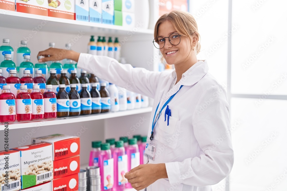 Young blonde girl pharmacist smiling confident working at pharmacy