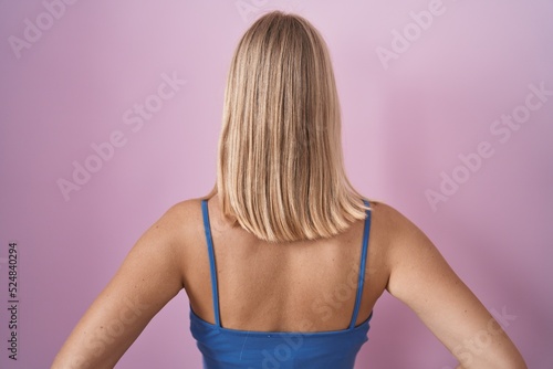 Young caucasian woman standing over pink background standing backwards looking away with arms on body