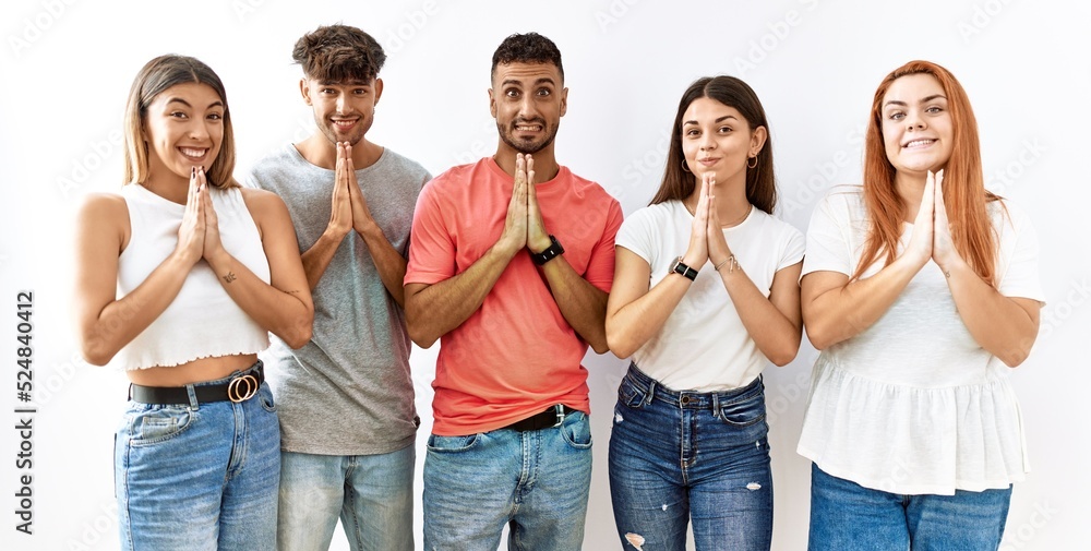 Obraz premium Group of young friends standing together over isolated background praying with hands together asking for forgiveness smiling confident.