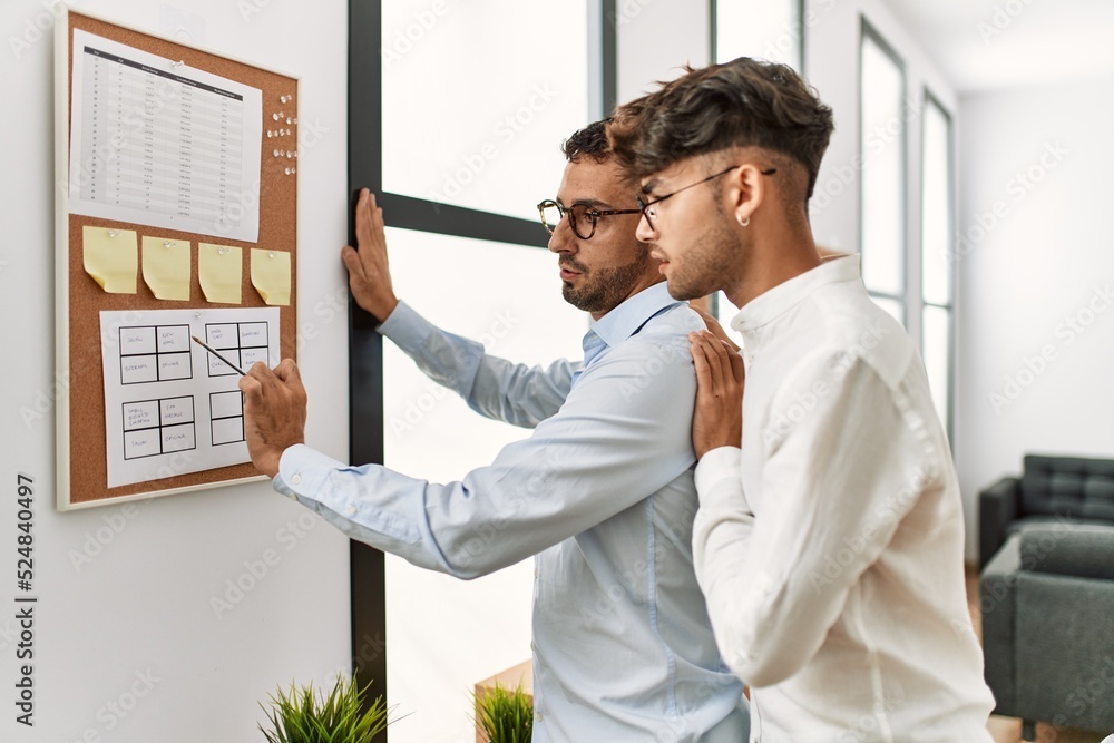 Fototapeta premium Two hispanic men couple writing on corkboard working at office