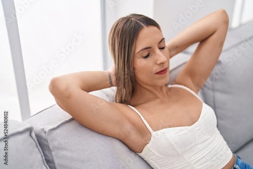 Young beautiful hispanic woman relaxed with hands on head sitting on sofa at home