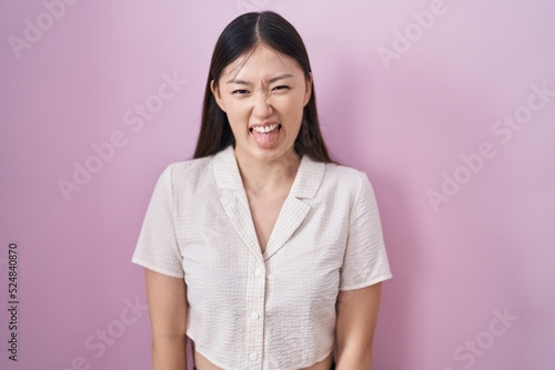 Chinese young woman standing over pink background sticking tongue out happy with funny expression. emotion concept. © Krakenimages.com