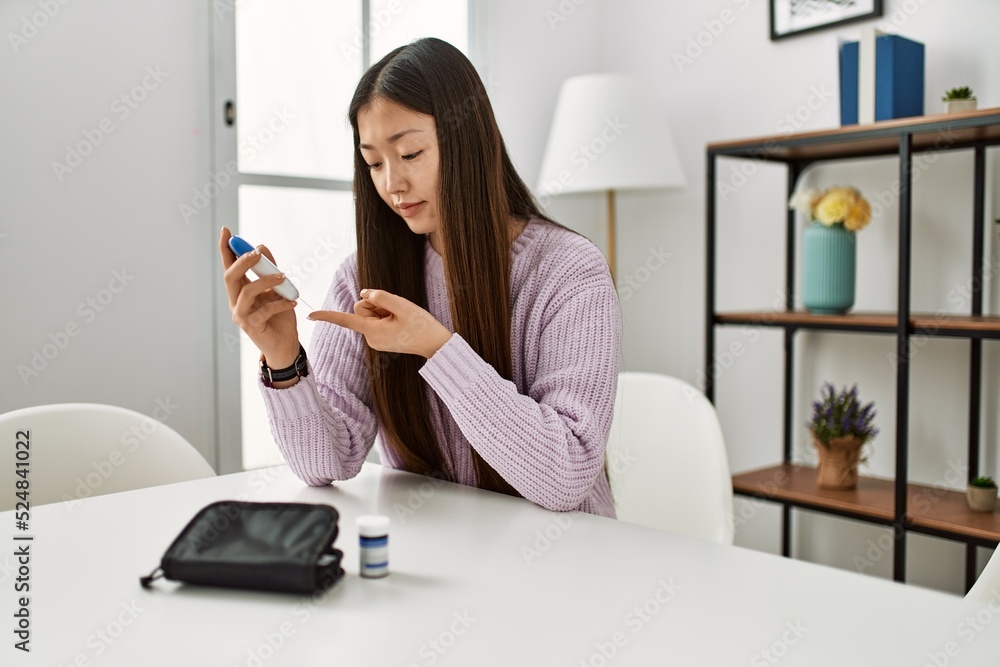 Young chinese girl measuring glucose sitting on the table at home. Young chinese girl measuring glucose sitting on the table at home.