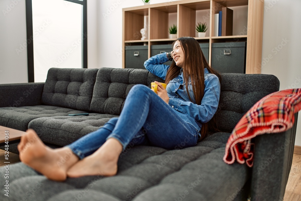 Young chinese girl drinking coffee lying on the sofa at home. Young chinese girl drinking coffee lying on the sofa at home.