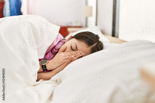 Young chinese girl sleeping on the bed covering face with hands at bedroom.