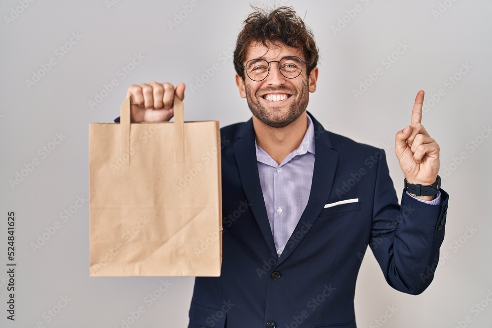 Hispanic business man holding delivery bag smiling happy pointing with hand and finger to the side Hispanic business man holding delivery bag smiling happy pointing with hand and finger to the side