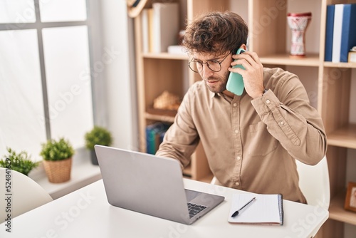 Young man business worker talking on smartphone using laptop at office