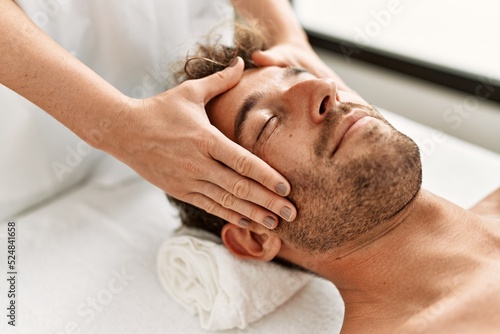 Young hispanic man having facial massage at beauty center