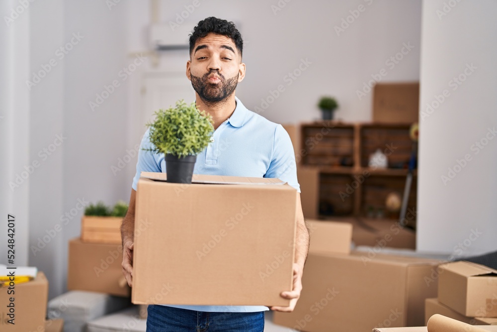 Hispanic man with beard moving to a new home holding box looking at the camera blowing a kiss being lovely and sexy. love expression. Hispanic man with beard moving to a new home holding box looking at the camera blowing a kiss being lovely and sexy. love expression.