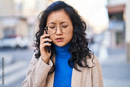 Young chinese woman worried talking on the smartphone at street