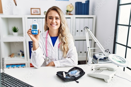 Young beautiful doctor woman holding glucose meter looking positive and happy standing and smiling with a confident smile showing teeth