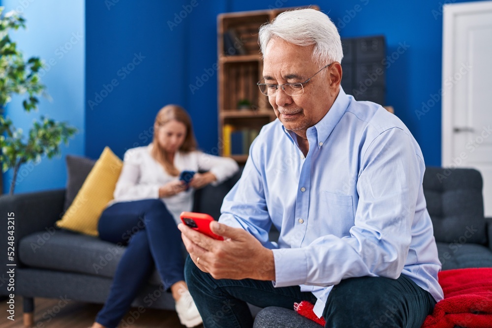 Middle age man and woman couple using smartphone sitting on sofa at home Middle age man and woman couple using smartphone sitting on sofa at home