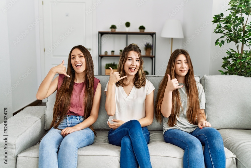 Group of three hispanic girls sitting on the sofa at home smiling doing phone gesture with hand and fingers like talking on the telephone. communicating concepts. Group of three hispanic girls sitting on the sofa at home smiling doing phone gesture with hand and fingers like talking on the telephone. communicating concepts.