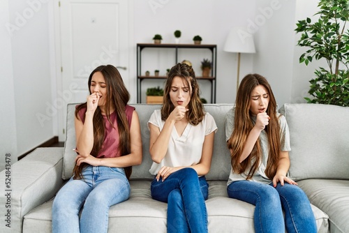 Group of three hispanic girls sitting on the sofa at home feeling unwell and coughing as symptom for cold or bronchitis. health care concept.