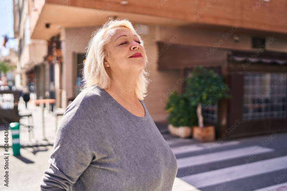 Middle age blonde woman smiling confident breathing at street