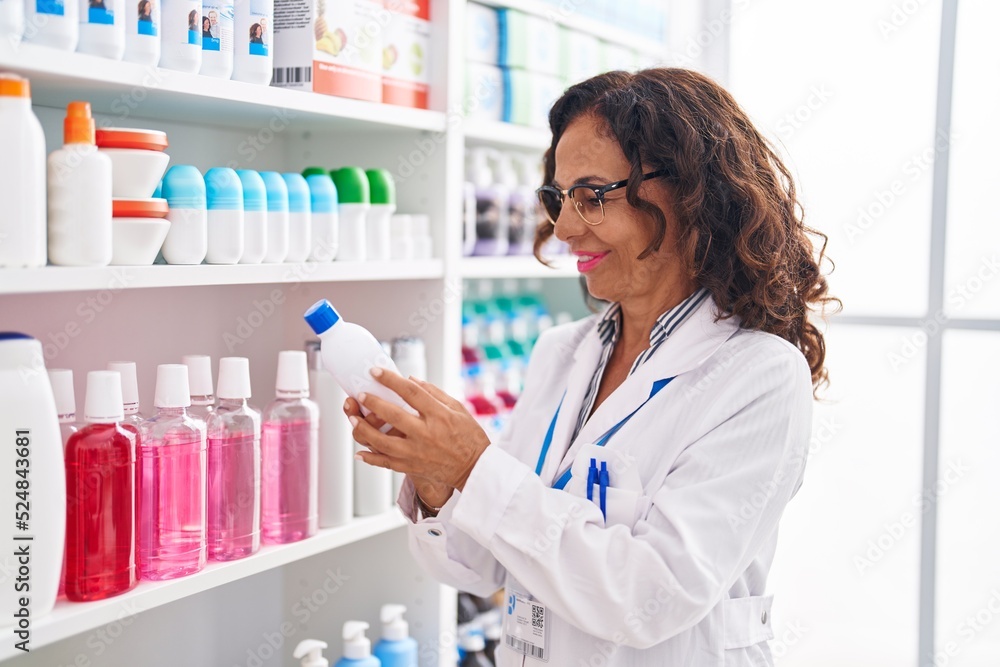 Middle age woman pharmacist holding medication bottle at pharmacy