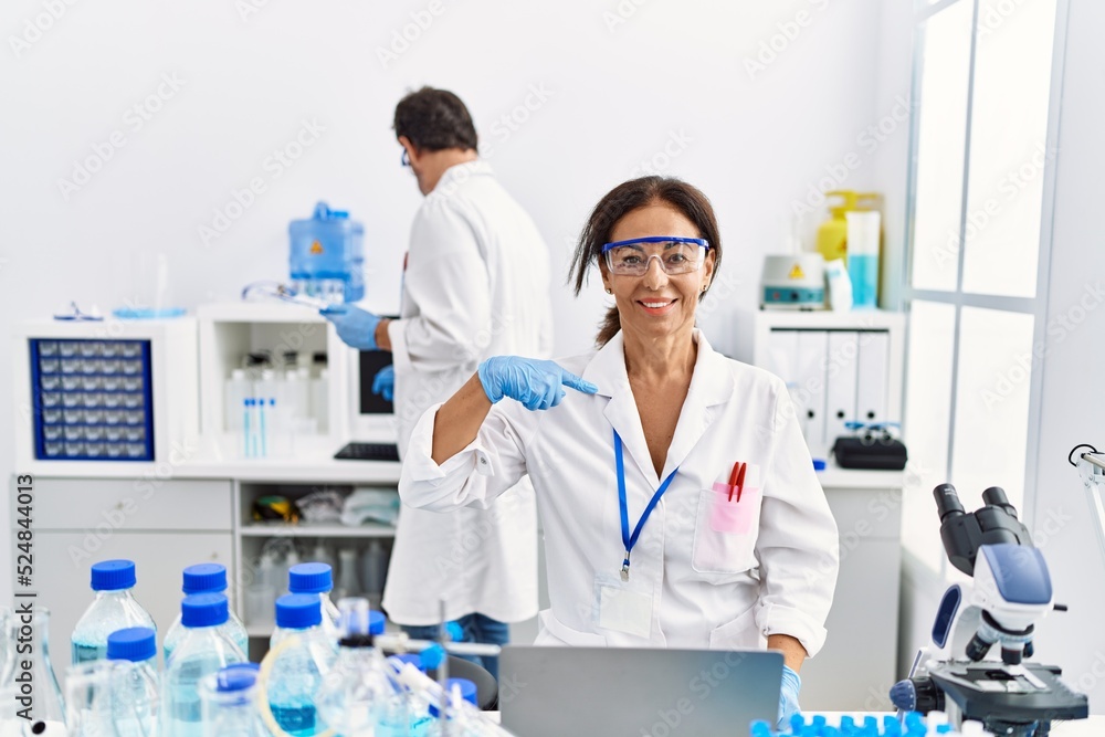 Middle age woman working at scientist laboratory pointing finger to one self smiling happy and proud