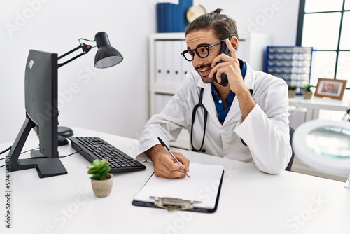 Handsome hispanic man writing presciption on the phone at hospital clinic