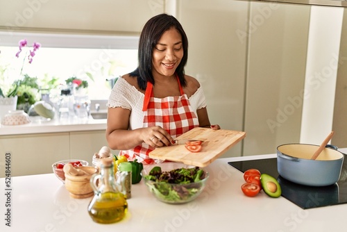 Hispanic brunette woman preparing green salad at the kitchen
