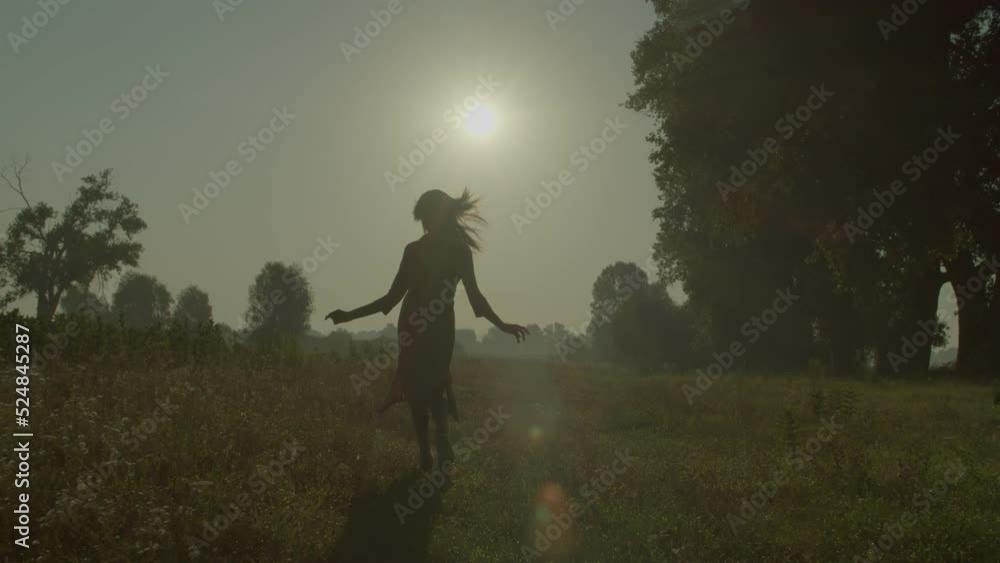Silhouette of joyful pretty black female in summer dress enjoying freedom and scenic nature, running along field, expressing carefree mood and happiness while relaxing in countryside at dawn. Silhouette of joyful pretty black female in summer dress enjoying freedom and scenic nature, running along field, expressing carefree mood and happiness while relaxing in countryside at dawn.