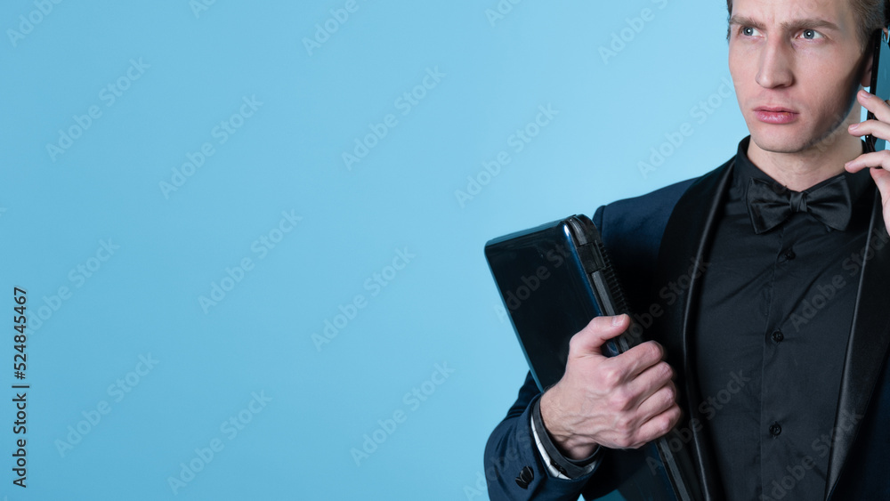 A successful and positive young man in a business suit with a laptop in his hands, talking on the phone, photo on blue A successful and positive young man in a business suit with a laptop in his hands, talking on the phone, photo on blue